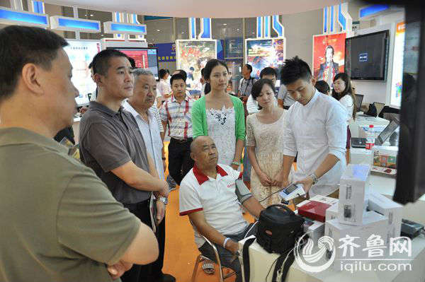 一位老人正在山东广电展区，体验新产品“老伴儿电视宝”的各种功能。