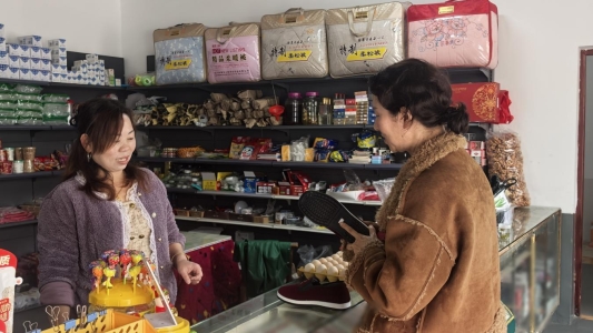 图为徐香荣向游客推介手工布鞋