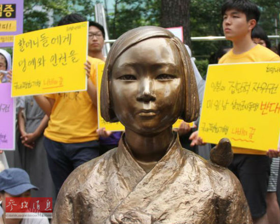 资料图：在韩国首尔的日本驻韩国大使馆前，韩国民众在慰安妇少女像旁手持标语参加抗议活动。