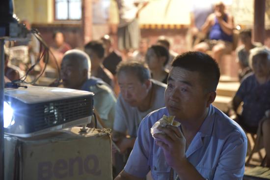 6月27日，在贾寨镇邢胡刘村，贾喜安趁电影放映期间，吃个烧饼作晚饭。