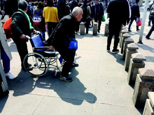 ▲济南站广场,隔离桩前,坐轮椅的老人吃力地站起身,等待其他人把轮椅抬过隔离桩。